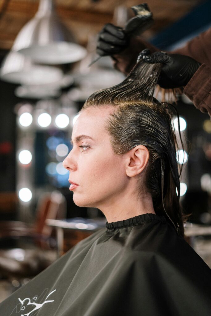 Professional hair stylist applying dye to woman's hair in a salon setting.