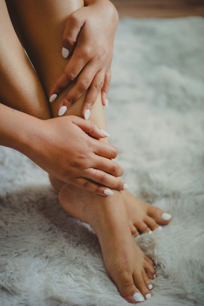 Aesthetic close-up of a woman's manicured hands and legs resting on a soft carpet.